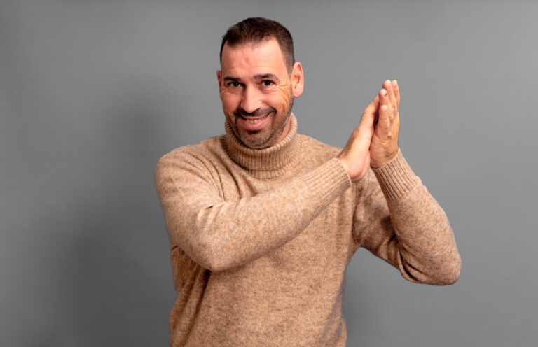 Bearded Hispanic Man Wearing A Beige Turtleneck Clapping His Han